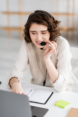 Wall Mural - smiling language teacher in headset talking near laptop and blank notebook while working at home.
