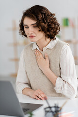 Wall Mural - curly brunette woman showing please gesture on sign language while having online lesson on blurred l