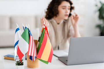 Wall Mural - selective focus of different international flags near laptop and blurred language teacher working at