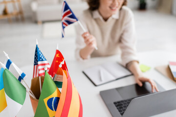Wall Mural - selective focus of international flags near teacher of foreign languages using laptop on blurred bac