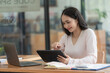 © Songsak C - An Asian businesswoman using a digital tablet while sitting at a work desk in an office