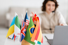 Selective Focus Of Various International Flags Near Blurred Laptop And Language Teacher Having Online Lesson At Home.
