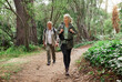 © Nina/peopleimages.com - Nature, forest and senior couple hiking for health, wellness and cardio exercise outdoor. Travel, trail adventure and elderly man and woman in retirement trekking in the woods for a hobby or workout.