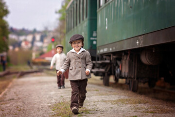 Two boys, dressed in vintage clothing and hat, with suitcase, on a railway station