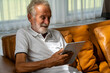 © jiradet_ponari - Caucasian old man smiling on the sofa Play tablet happily in the living room.