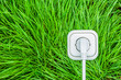 Weisse Steckdose mit Stromstecker und Kabel auf grünem Gras
