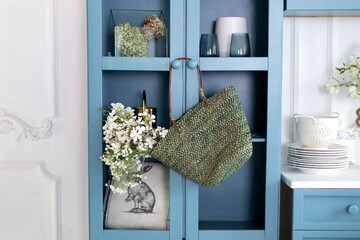 Wall Mural - The minimalist interior design of the Scandinavian kitchen is decorated with a hanging wicker bag with flowers. On Wooden blue cupboard hanging wicker basket with white flowers. 