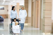 © ronnachaipark - Female pediatrician doctor and child patient on wheelchair with her mother in the health medical center