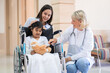 © ronnachaipark - Female pediatrician doctor and child patient on wheelchair with her mother in the health medical center