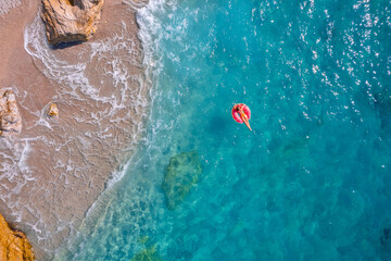 Aerial top view young woman swimming with donut pink inflatable swim ring in blue sea. Concept tropical paradise travel relax