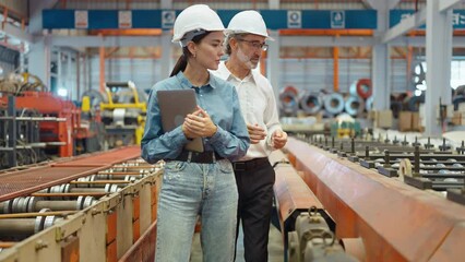 Wall Mural - Two professional engineer man and woman manager leader wearing helmet and holding laptop walking in factory talking and discussing for work