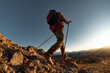 © cppzone - Hiker with backpack walk uphill in mountains. Active tourist silhouette goes with hiking poles at sunset