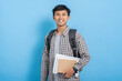 © Molas Images - Young asian college student carrying books and backpack isolated over blue background