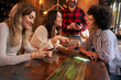 © CarlosBarquero - Group young girls look at cafeteria menu on cell phones to order something to take from waiter. Women happily decide what to drink at bar. People sitting at the table in their free time after work.