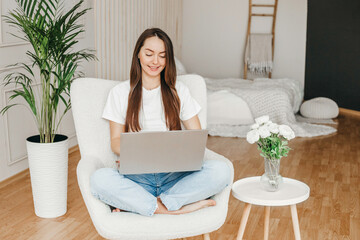 Wall Mural - Happy casual beautiful woman working on a laptop sitting on the bed in her room