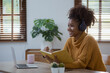 © SOMKID - Young African woman holding a book with earphones sitting on sofa at home, young woman stay at home concept.