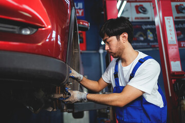 Asian auto mechanic in car garage. Vehicle service personnel are inspecting cars in mechanic factory with confidence in car engine repairs. Asian mechanic with equipment to fix cars in the service.