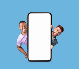 Wall Mural - Mobile Ad. Two Cheerful Men Peeking Out Behind Big Blank Smartphone