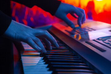 close-up of the hands of a musician playing a synthesizer against the backdrop of concert spotlights