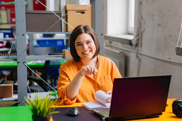 a brunette woman in an orange blouse works on a laptop at desk in the office