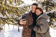 © CinemaF - A happy young couple takes a photo together in front of snow-covered trees. Smiling young people decide to take a picture while walking on a day walk in a snow-covered park.