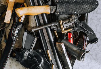 Weapons of various calibers, a rifle, a retro revolver with cartridges, barrels, pistols, hunting knives, parts and accessories, ammunition lie on the table. Photography, firearms concept.