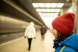 a smiling boy in a winter jacket and hat is waiting for an approaching train on a subway platform