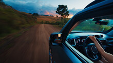 Woman Steers The Car On A Rural Road At Vivid Sunset. Solo Female Traveler Drives The Car On An Empty Unpaved Road