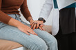 © Odua Images - a female doctor in doctor's coat put her hand above the hand of the female patient in brown clothes and denim pants