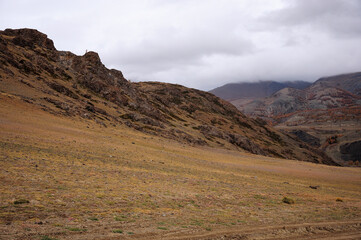 Wall Mural - The gentle slope of a high rocky hill under thunderclouds in the autumn dried steppe.