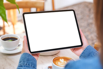 Mockup image of a woman holding digital tablet with blank white desktop screen with cake and coffee cup on the table in cafe