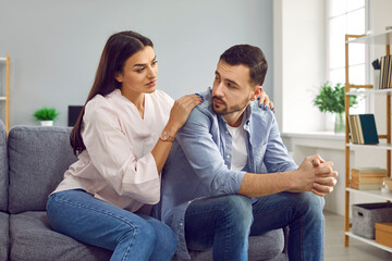 Wall Mural - Attractive wife hugging husband from back to comfort or apologize. Young woman hugging upset man, expressing understanding, saying sorry, showing support. Couple sitting on sofa at home