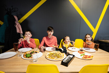 Four kids eating italian pizza in pizzeria. Children eat at cafe.