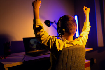 Young excited boy gamer with headphone playing video game on laptop at home.