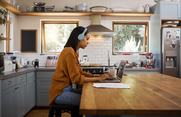 Wall Mural - Home, remote work and business woman on laptop for research project, strategy and planning in kitchen. Freelancer, focus and girl with headphones for music with documents, computer and working online