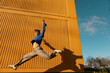 © VISTA by Westend61 - Young woman jumping in front of cargo container