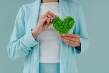 Woman Holding Green Heart Shape Moss Against Blue Background