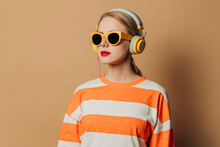 Woman Wearing Headphones And Sunglasses Standing Against Brown Background