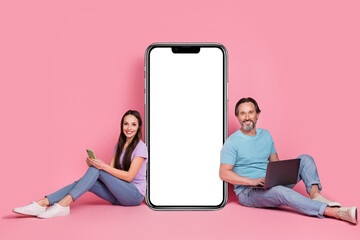 Wall Mural - Photo of lovely married couple spend free time surfing in digital gadget lean on huge phone panel isolated on pink color background