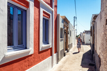 Wall Mural - Woman in long dress walking through an alley in greek village Koskinou in Rhodes island in Greece