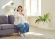 © Studio Romantic - Portrait of a young plump overweight fat woman sitting on the couch in the living room at home putting a hand on her chest suffering from heart problems. Obesity problems and healthcare concept.