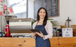 © David - Startup successful small business owner sme beauty girl stand with tablet smartphone in coffee shop restaurant. Portrait of asian tan woman barista cafe owner. SME entrepreneur seller business concept