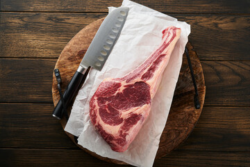 Wall Mural - Fresh tomahawk raw steak. Dry aged raw tomahawk beef steak with herbs and salt on old wooden background. Preparing to grill.  Top view and copy space.