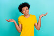 Portrait of confused funny guy afro hairdo wear yellow t-shirt shrugging shoulders has no idea isolated on shine teal color background
