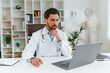 © standret - Sitting by a table. Doctor in formal clothes is working in the cabinet