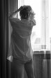 Woman at the window in a pink shirt. A woman looking out the window in a men's shirt and briefs. Black and white version