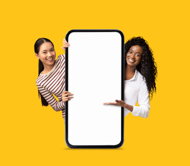 Wall Mural - Beautiful Multiethnic Women Holding And Pointing At Big Smartphone With Blank Screen