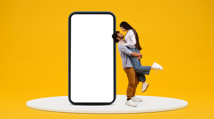 Wall Mural - Happy millennial indian guy hold girlfriend, have fun near huge phone with blank screen