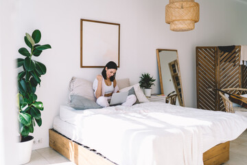 Wall Mural - Cheerful woman using laptop and sitting in bedroom