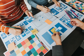 Close up ux developer and ui designer brainstorming about mobile app interface wireframe design on table with customer breif and color code at modern office.Creative digital development agency